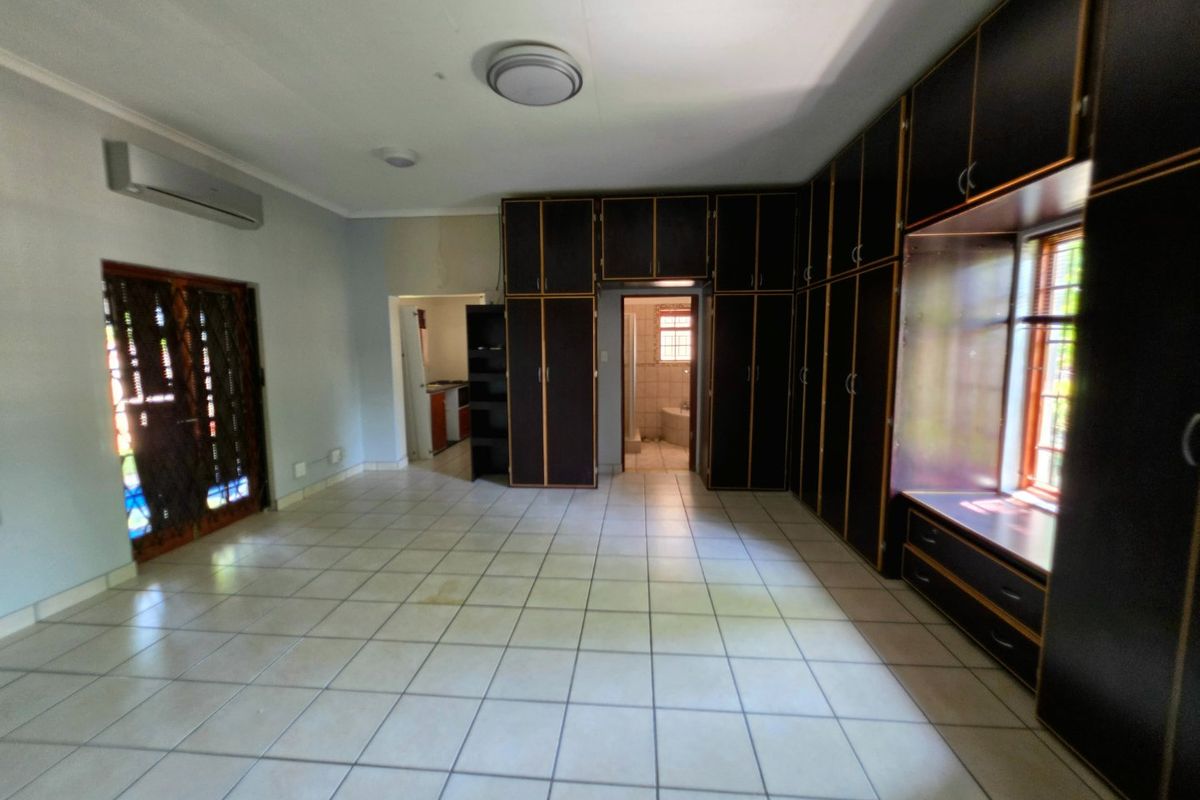 Spacious bedroom featuring extensive built-in cabinetry, tiled flooring, an integrated air conditioning unit, and direct access to an en-suite bathroom.