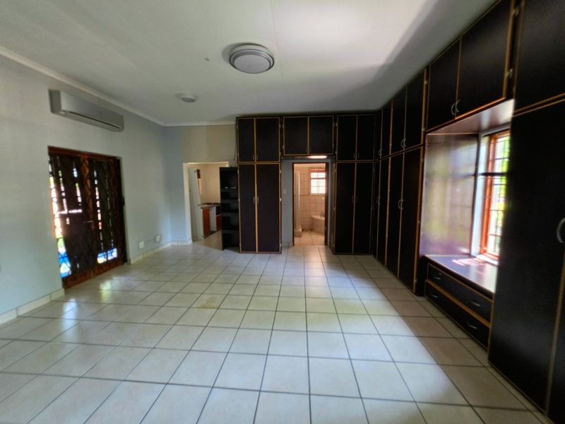 Spacious bedroom featuring extensive built-in cabinetry, tiled flooring, an integrated air conditioning unit, and direct access to an en-suite bathroom.
