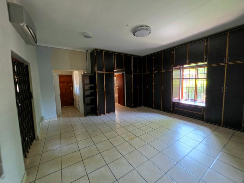 Spacious bedroom featuring extensive built-in cabinetry, tiled flooring, and an integrated air conditioning unit, offering a blank canvas for personalization.