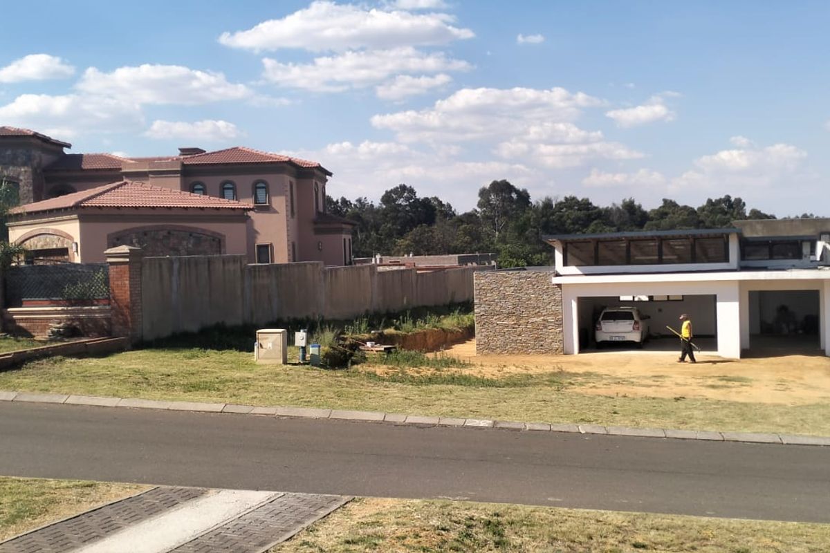 A street-level view of a residential property featuring a paved driveway, stone-clad garage structure, and surrounding boundary walls in a suburban setting.