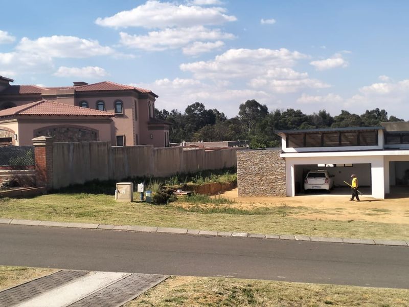 A street-level view of a residential property featuring a paved driveway, stone-clad garage structure, and surrounding boundary walls in a suburban setting.