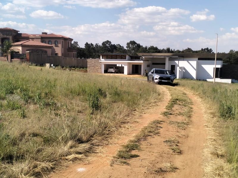A view of a vacant residential plot featuring a dirt driveway leading towards a neighboring property.