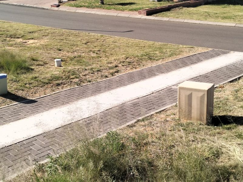 A view of the street frontage showing a paved driveway entrance and utility connection points on a vacant residential plot.