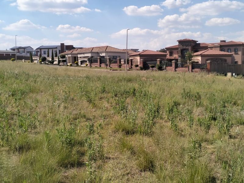 A wide-angle view of a vacant residential plot featuring natural grassland, situated within an established residential estate.