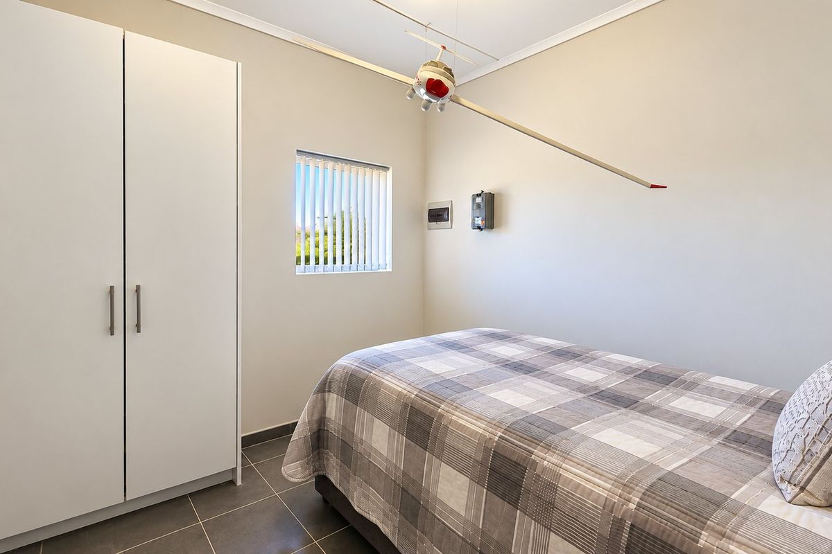 A clean bedroom featuring tiled flooring, a built-in wardrobe, and a window fitted with vertical blinds.