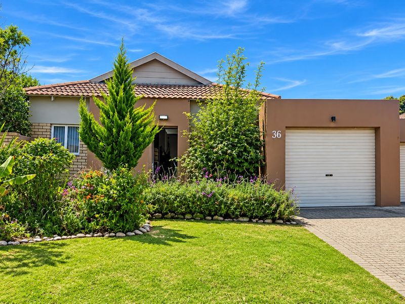 A well-maintained single-story residential property featuring a paved driveway, double garage with roller doors, and a neatly landscaped front garden.