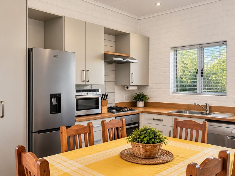 A well-maintained open-plan kitchen featuring modern cabinetry, timber countertops, a gas hob, and a bright, functional layout with a painted brick feature wall.