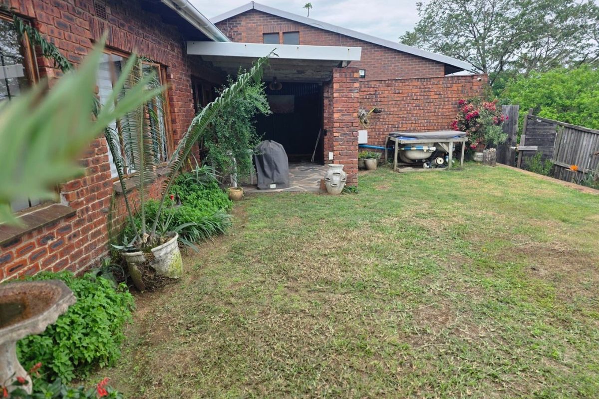 A rear view of the property featuring a face brick facade, a covered patio area with paved flooring, and a grass lawn.