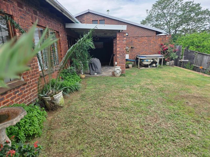 A rear view of the property featuring a face brick facade, a covered patio area with paved flooring, and a grass lawn.
