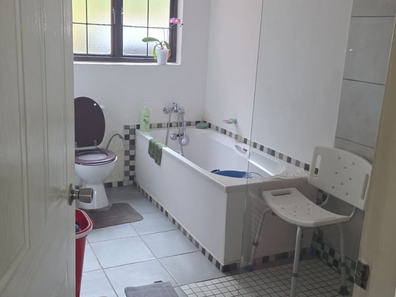 A functional bathroom featuring a bathtub, toilet, and a glass-enclosed shower area with tiled flooring and natural light from a window.