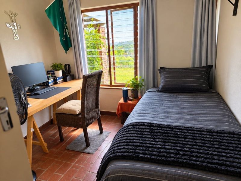 A compact bedroom featuring terracotta tile flooring and a timber frame window with natural light.