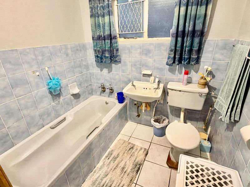 A functional bathroom featuring a bathtub, wall-mounted basin, and toilet, finished with light blue ceramic wall tiles and white floor tiles.