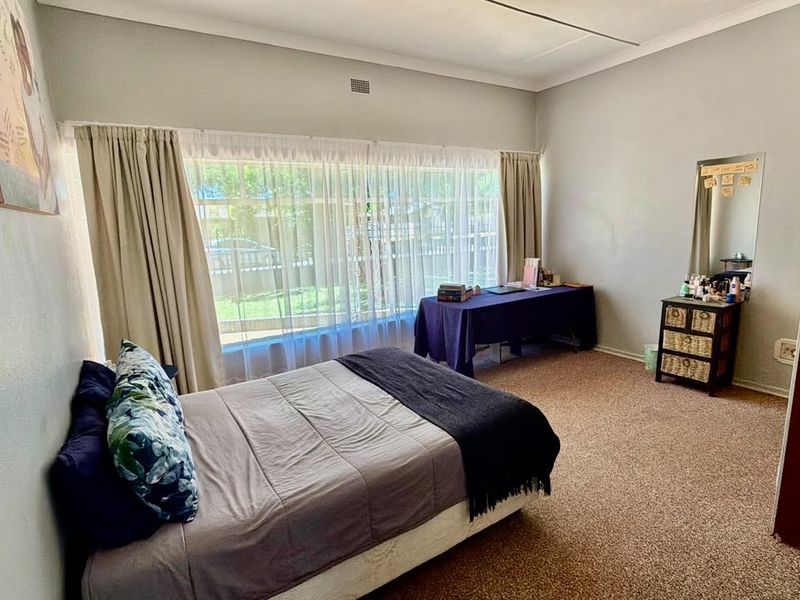 A spacious bedroom featuring carpeted flooring, a large window with natural light, and a built-in cupboard.