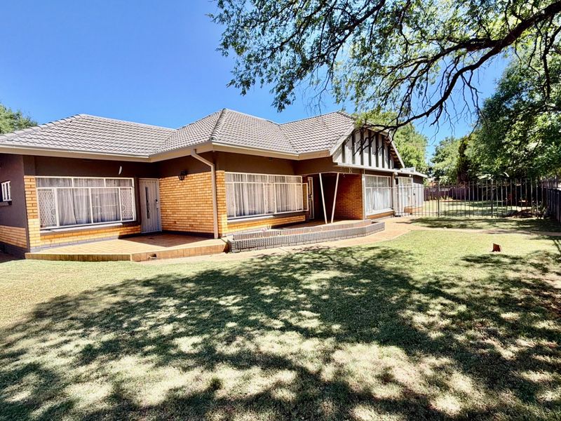 A well-maintained single-story house featuring a tiled roof, brick exterior, and a spacious front garden with paved patio area.