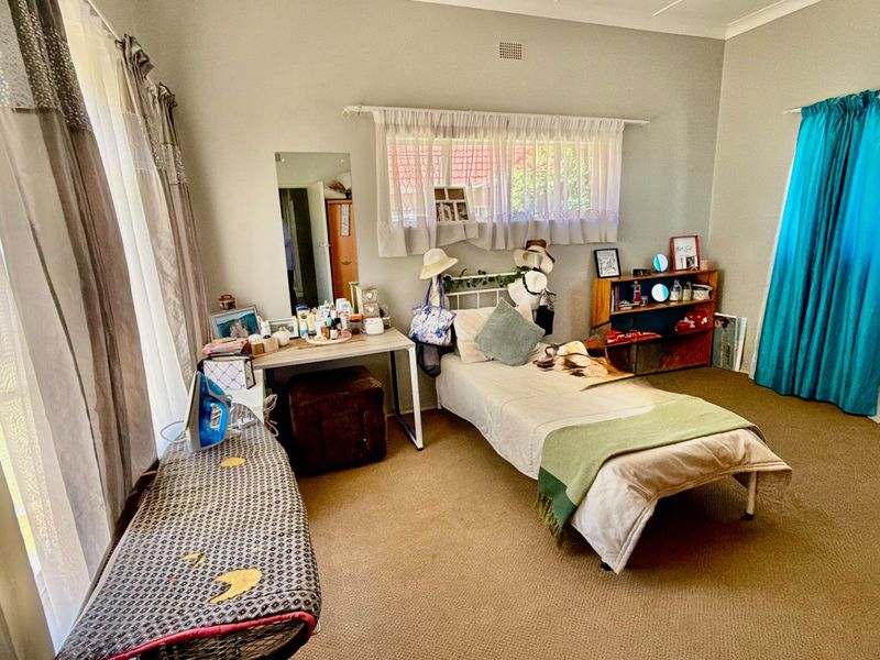 A spacious bedroom featuring neutral wall tones, carpeted flooring, and dual window treatments, offering a functional layout with ample natural light.