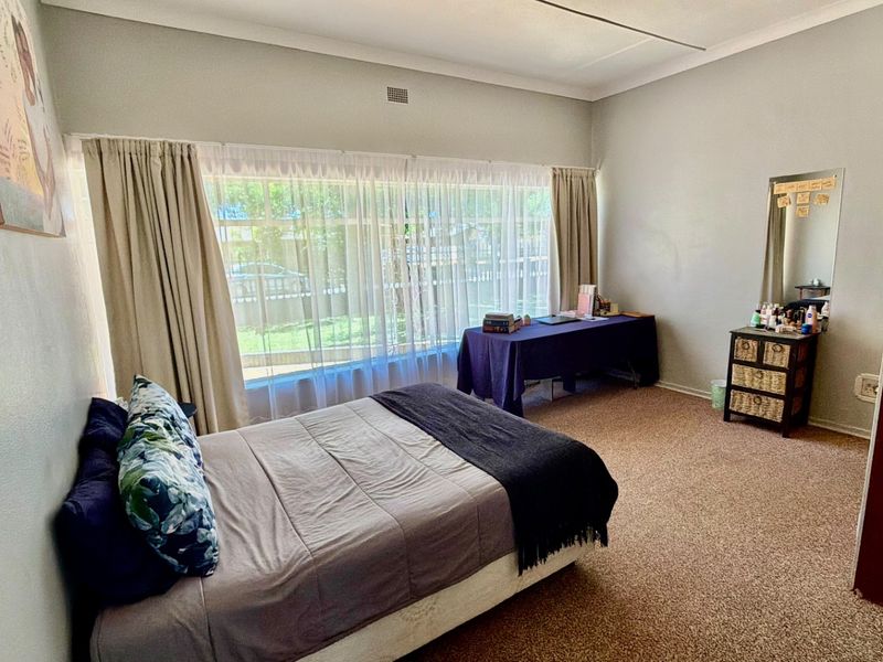 A spacious bedroom featuring large windows that provide ample natural light, neutral wall finishes, and carpeted flooring.