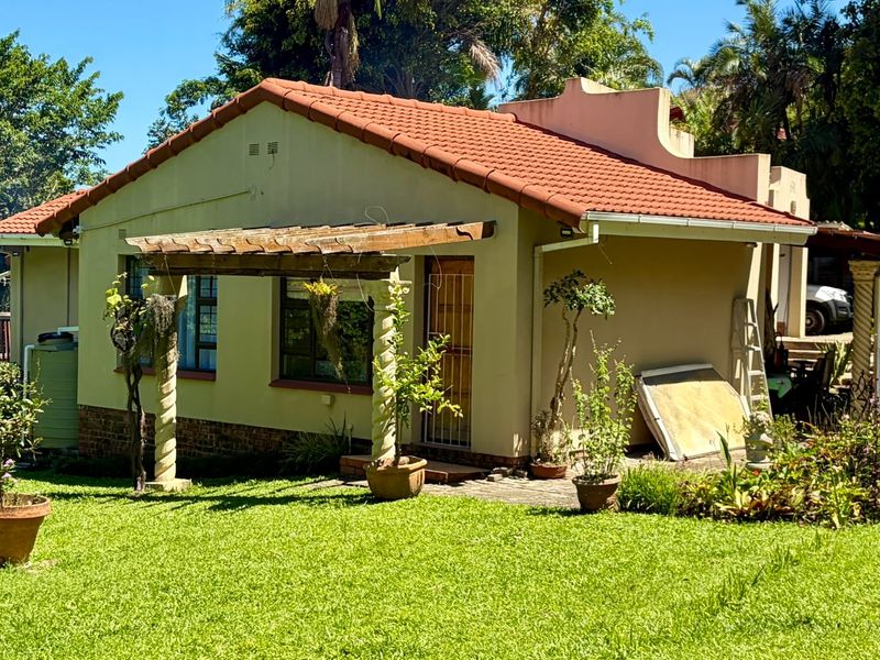 Rear view of the house featuring a terracotta tiled roof, a wooden pergola, and a well-maintained garden setting with established landscaping.