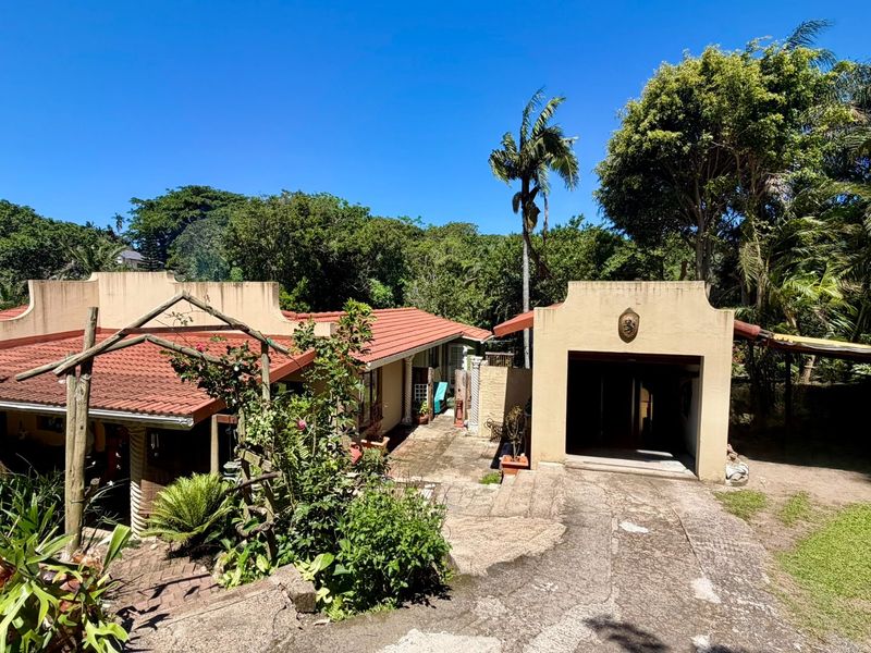 Front view of a single-story house featuring a terracotta tiled roof, a detached garage, and a paved driveway set within a mature garden.