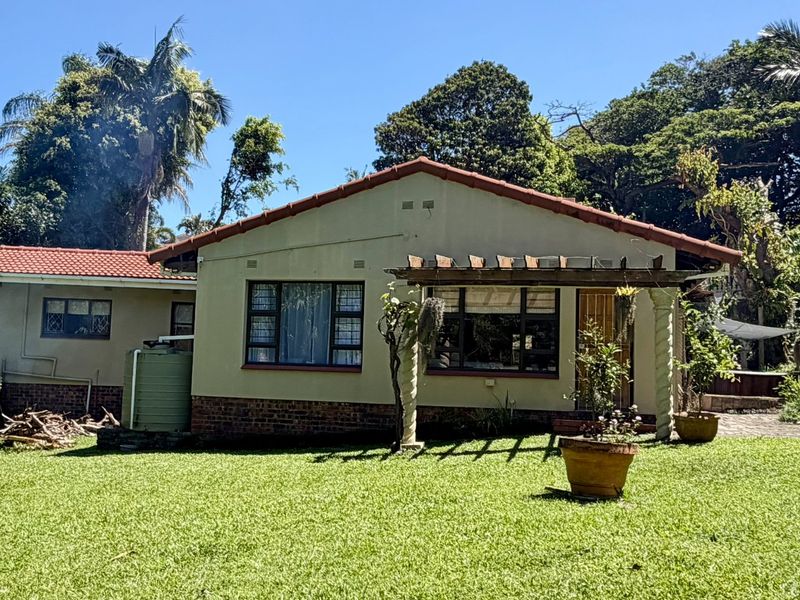 Rear view of a single-story house featuring a tiled roof, brick base, and a wooden pergola overlooking a spacious garden area.
