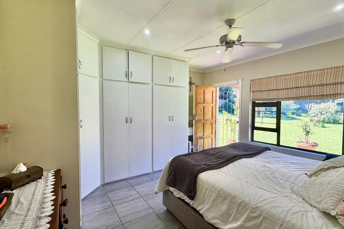 A bedroom featuring built-in cupboards, tiled flooring, a ceiling fan, and direct access to the garden through a security gate.