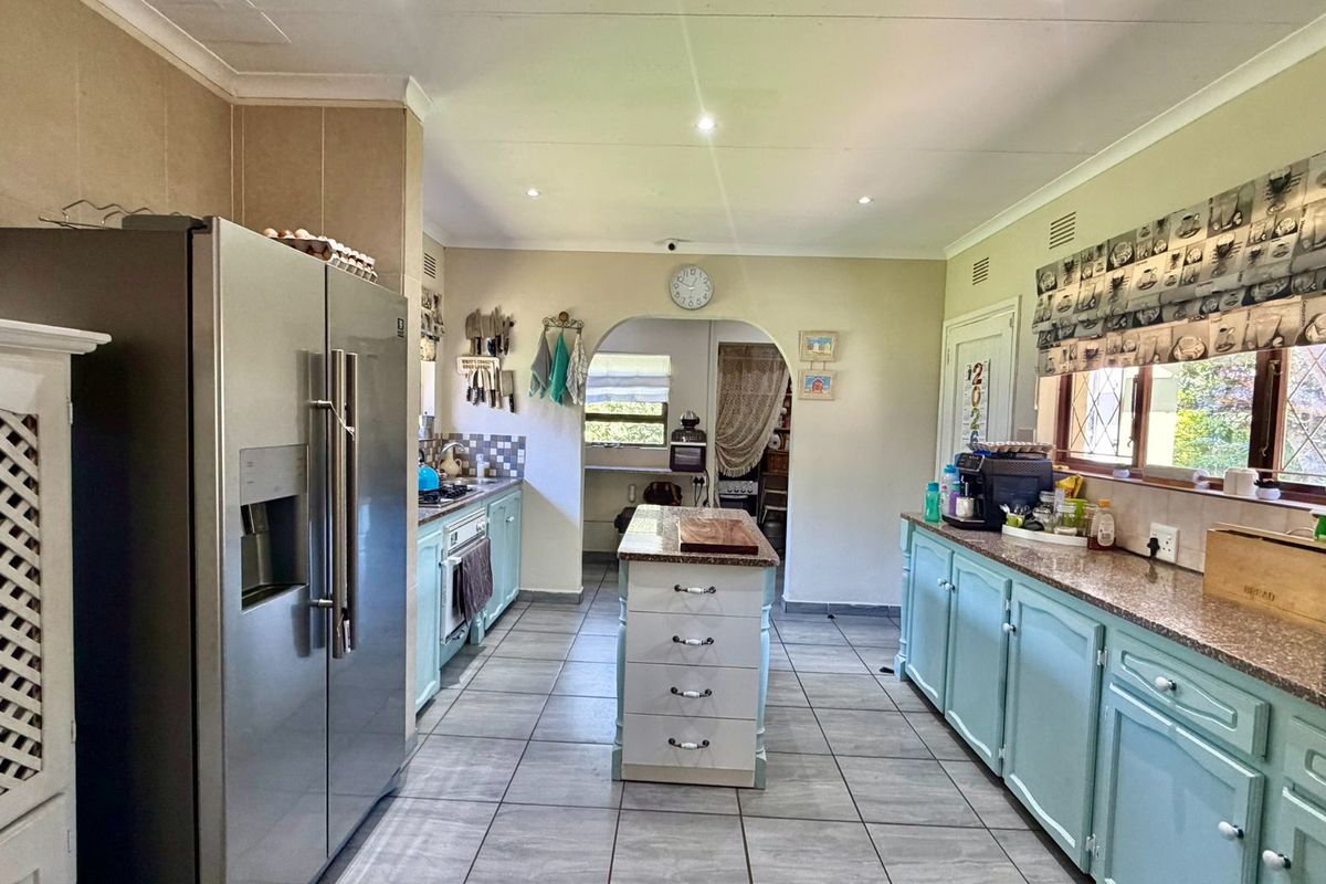 Spacious kitchen featuring a central island, granite countertops, light blue cabinetry, and tiled flooring, with an open archway leading to an adjacent utility area.