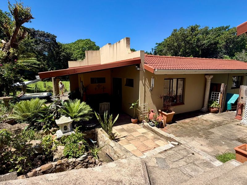 Rear exterior view of the property featuring a covered patio, terracotta roof tiles, and a landscaped garden area with stone features.