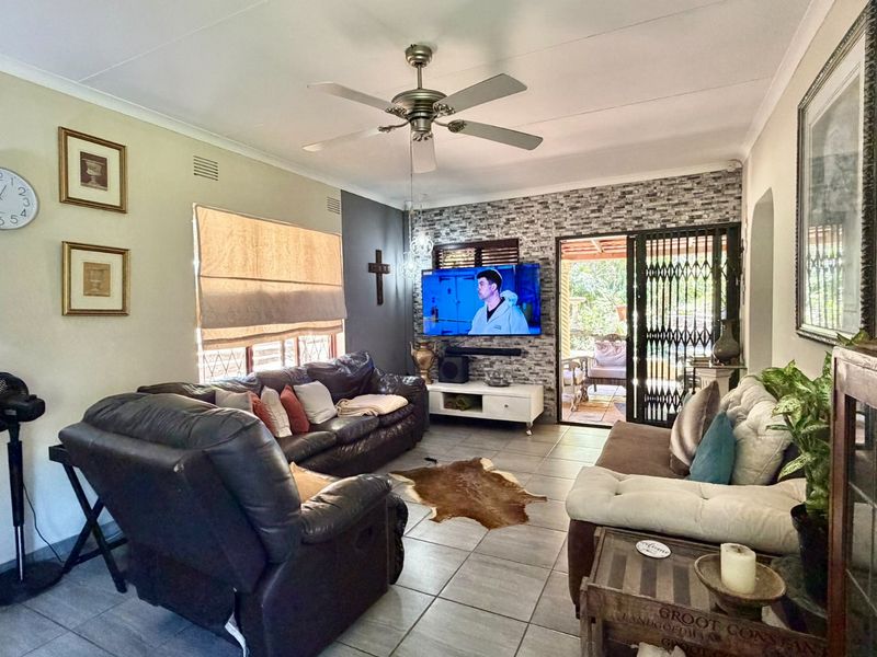 A comfortable living room featuring tiled flooring, a ceiling fan, and a stone veneer feature wall with direct access to an outdoor patio area.