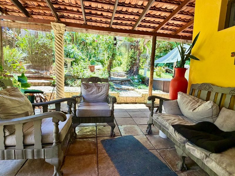 A covered outdoor patio area featuring tiled flooring, a decorative column, and an exposed timber beam ceiling, overlooking a lush garden space.