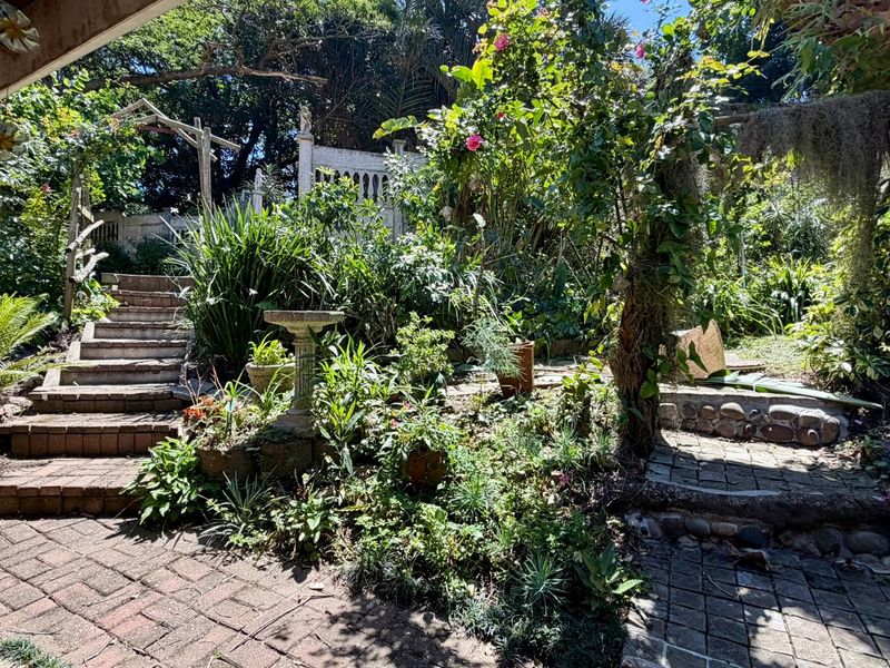 A lush, established garden featuring brick paved pathways, stone stairs, and mature landscaping with stone retaining elements.