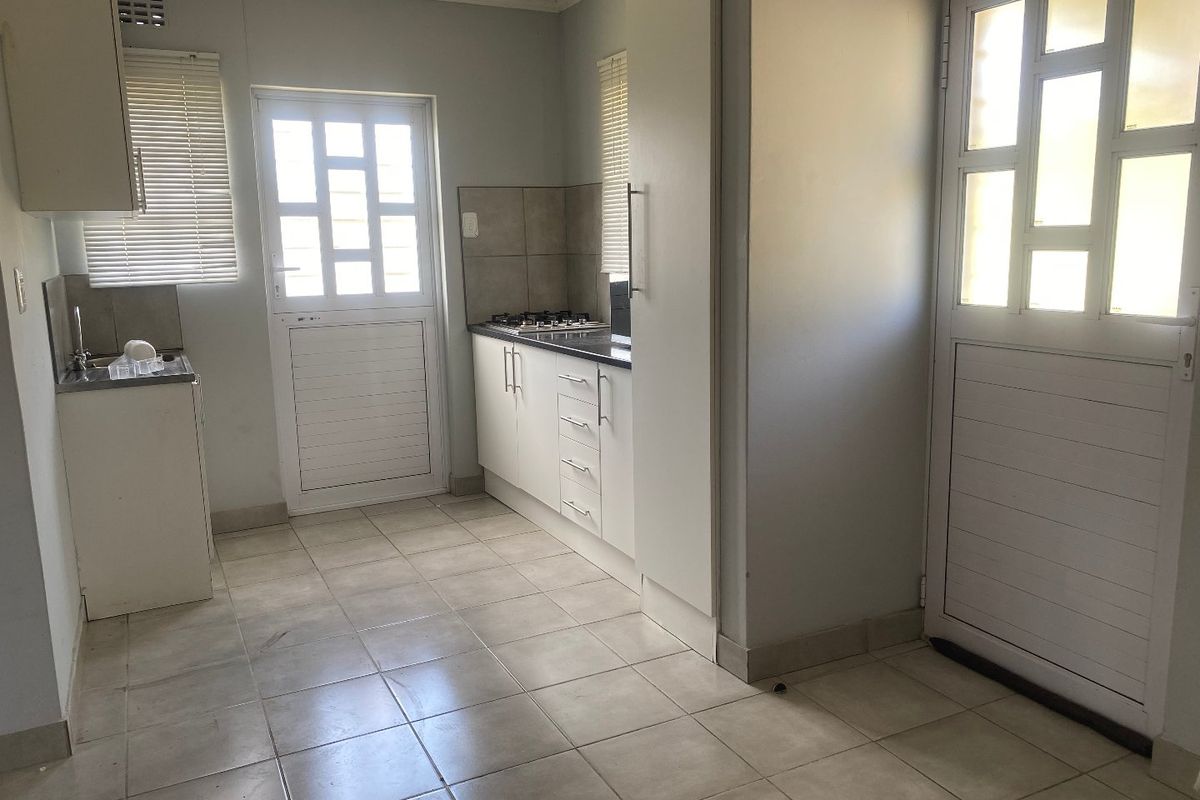 A functional kitchen featuring white built-in cabinetry, a gas hob, tiled flooring, and a tiled backsplash, offering a clean and practical workspace.