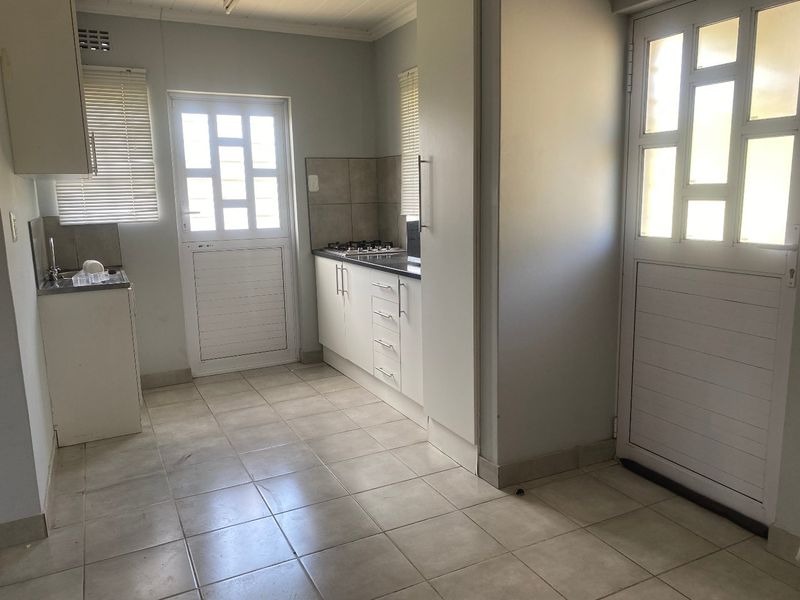 A functional kitchen featuring white built-in cabinetry, a gas hob, tiled flooring, and a tiled backsplash, offering a clean and practical workspace.