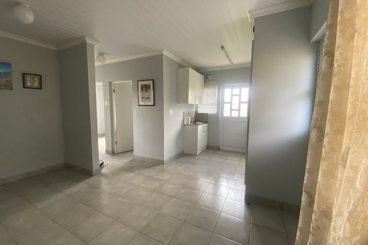 An open-plan living area featuring tiled flooring, a tongue and groove ceiling, and a compact kitchenette with built-in cabinetry and a sink.