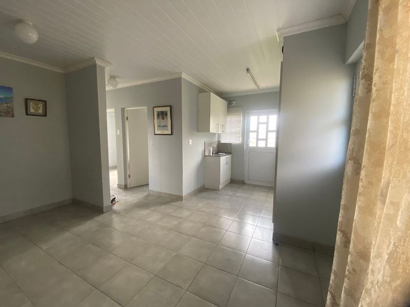 An open-plan living area featuring tiled flooring, a tongue and groove ceiling, and a compact kitchenette with built-in cabinetry and a sink.