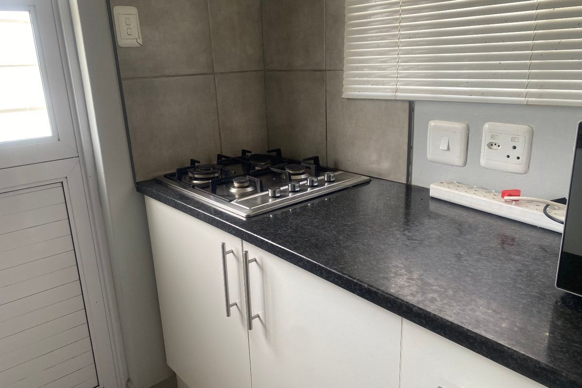 A compact kitchen area featuring a built-in gas hob, dark granite countertops, white cabinetry, and tiled splashbacks.