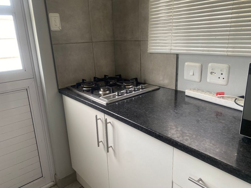 A compact kitchen area featuring a built-in gas hob, dark granite countertops, white cabinetry, and tiled splashbacks.