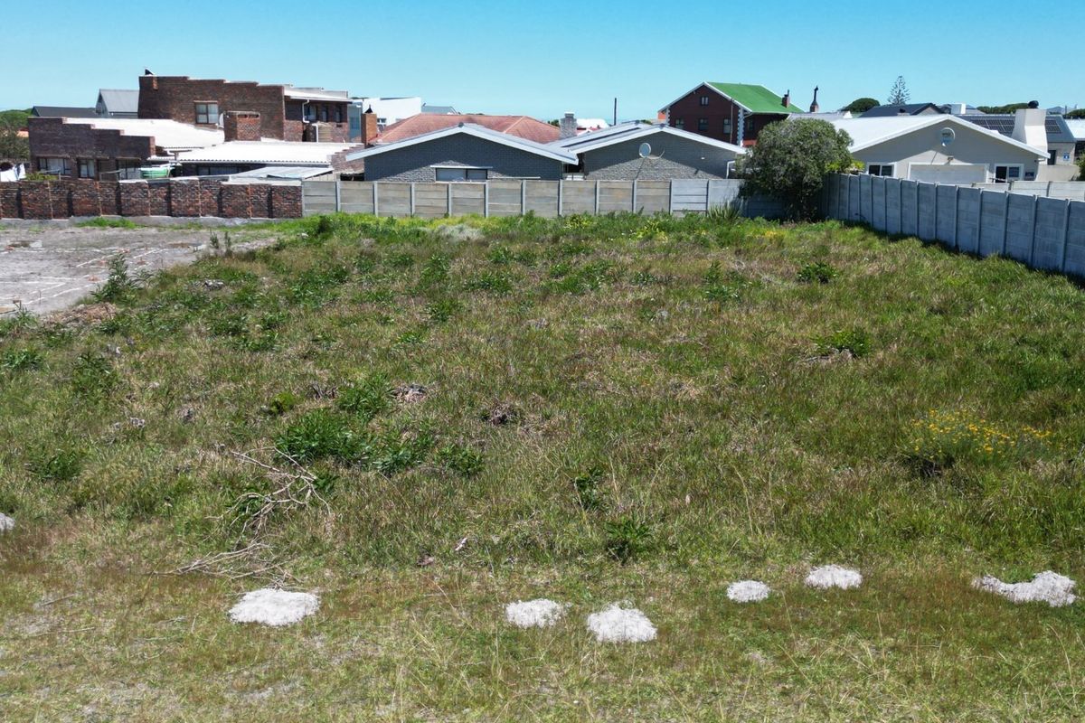 A vacant residential plot featuring natural grass cover and enclosed by precast concrete and brick boundary walls in a developed neighborhood.