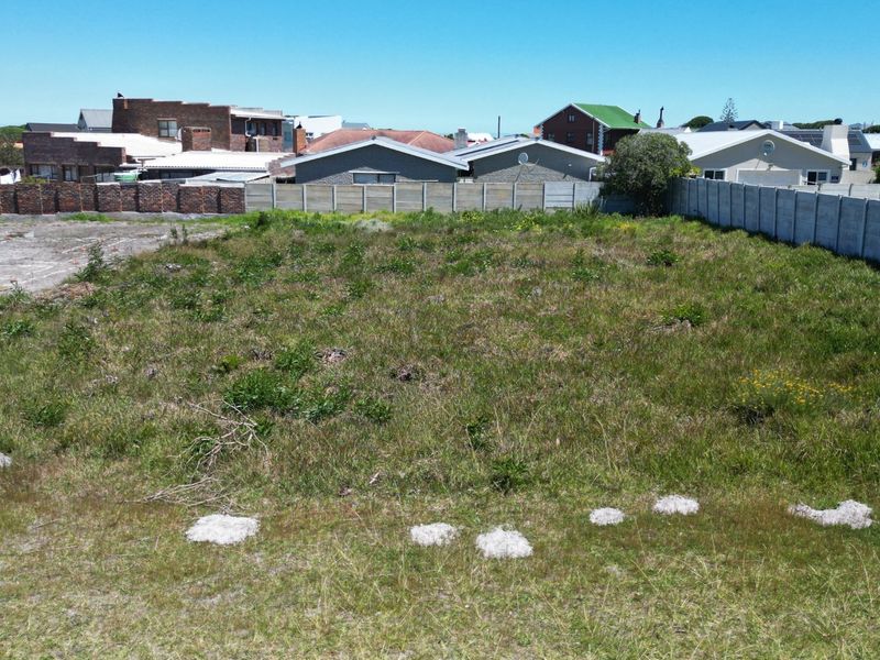 A vacant residential plot featuring natural grass cover and enclosed by precast concrete and brick boundary walls in a developed neighborhood.