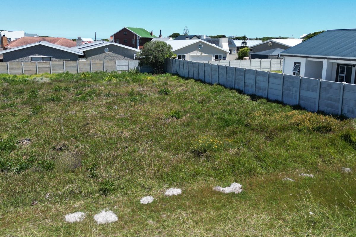 A vacant residential plot featuring natural grass coverage and enclosed by precast concrete boundary walls in a established neighborhood setting.