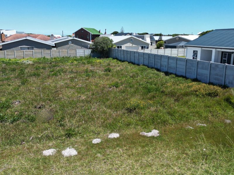 A vacant residential plot featuring natural grass coverage and enclosed by precast concrete boundary walls in a established neighborhood setting.