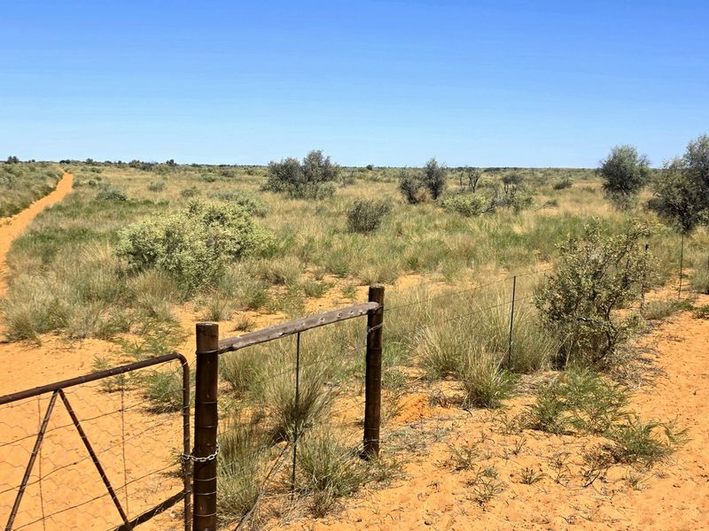 Expansive view of open farm land featuring natural vegetation, sandy terrain, and traditional wire fencing with a metal gate.