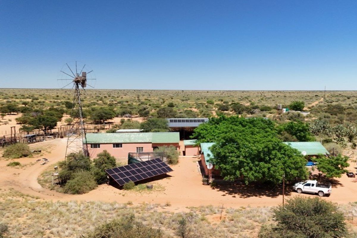 Aerial view of a farmstead featuring a windmill, solar panel array, and multiple outbuildings set within a vast rural landscape.