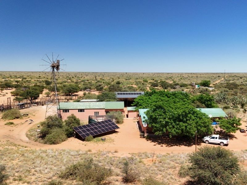 Aerial view of a farmstead featuring a windmill, solar panel array, and multiple outbuildings set within a vast rural landscape.
