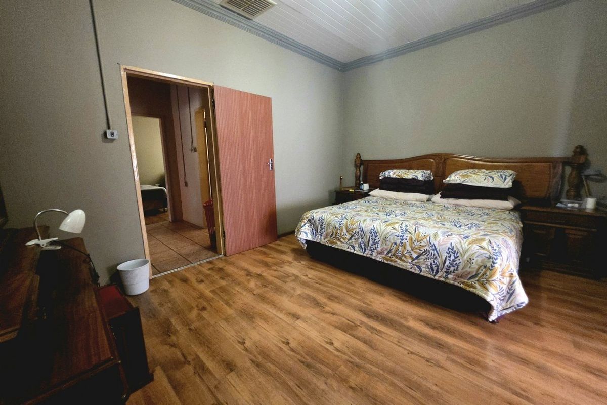Spacious bedroom featuring laminate flooring, a timber ceiling with coving, and direct access to an adjoining room.