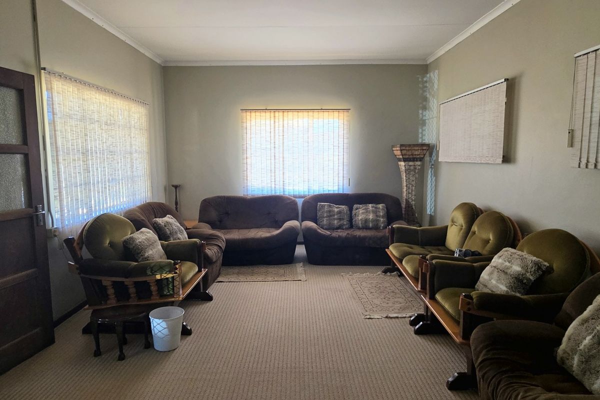 A spacious living room featuring neutral wall tones, carpeted flooring, and multiple windows fitted with venetian blinds.