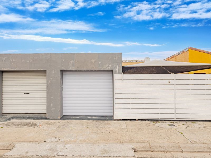 Exterior view of a double garage featuring roller shutter doors and a white slatted privacy fence, situated along a concrete driveway.