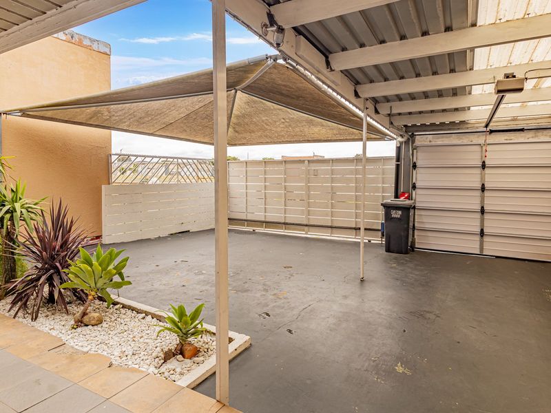 A covered outdoor patio area featuring a shade sail, concrete flooring, and a raised garden bed, providing a functional space for outdoor living.