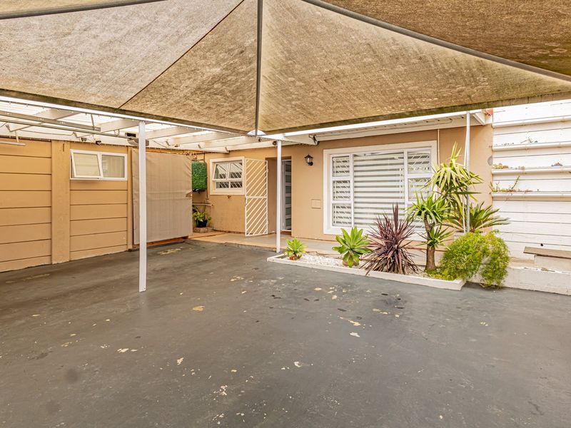 A covered outdoor patio area featuring a shade sail, paved flooring, and a built-in planter box, providing a functional space for outdoor living.