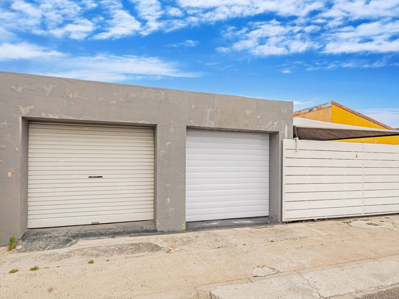 Exterior view of a double garage featuring roller doors and a side privacy screen, showing signs of wear on the concrete facade and driveway.