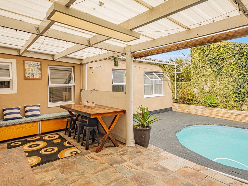 Covered outdoor patio area featuring tiled flooring, built-in bench seating, and direct access to a swimming pool with a stone-walled garden backdrop.