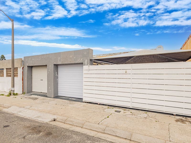 Front exterior view of the property featuring roller garage doors, a white horizontal slat fence, and a shade sail over the driveway area.
